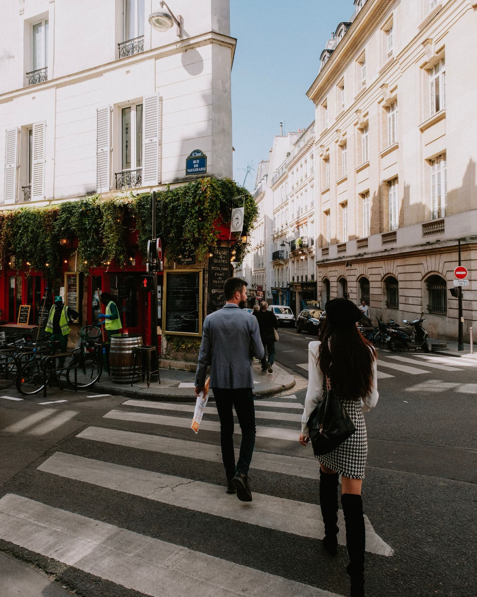 Un homme et une femme traversent une rue devant des immeubles parisiens
